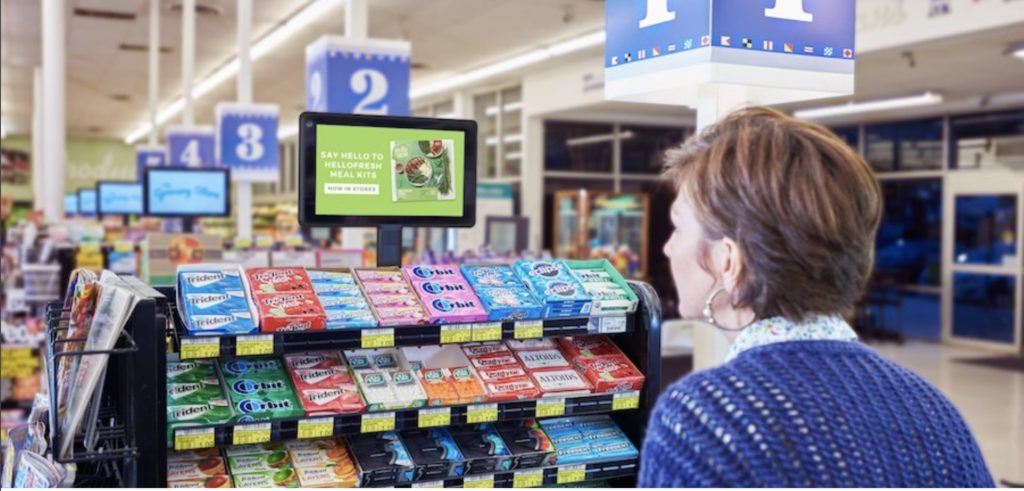 Woman looking at sign in grocery store. Digital OOH is here to stay!