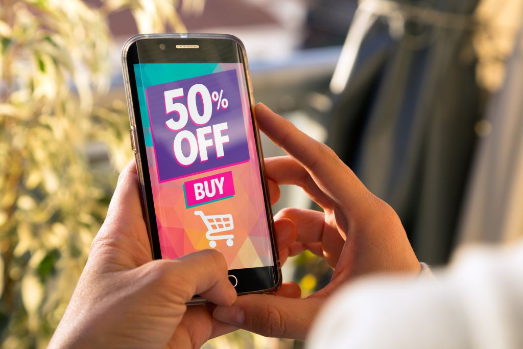 50% OFF Sale. Girl holding a smartphone with a 50% discount advertising on the screen. Marketing, ecommerce, cell phone publicity.