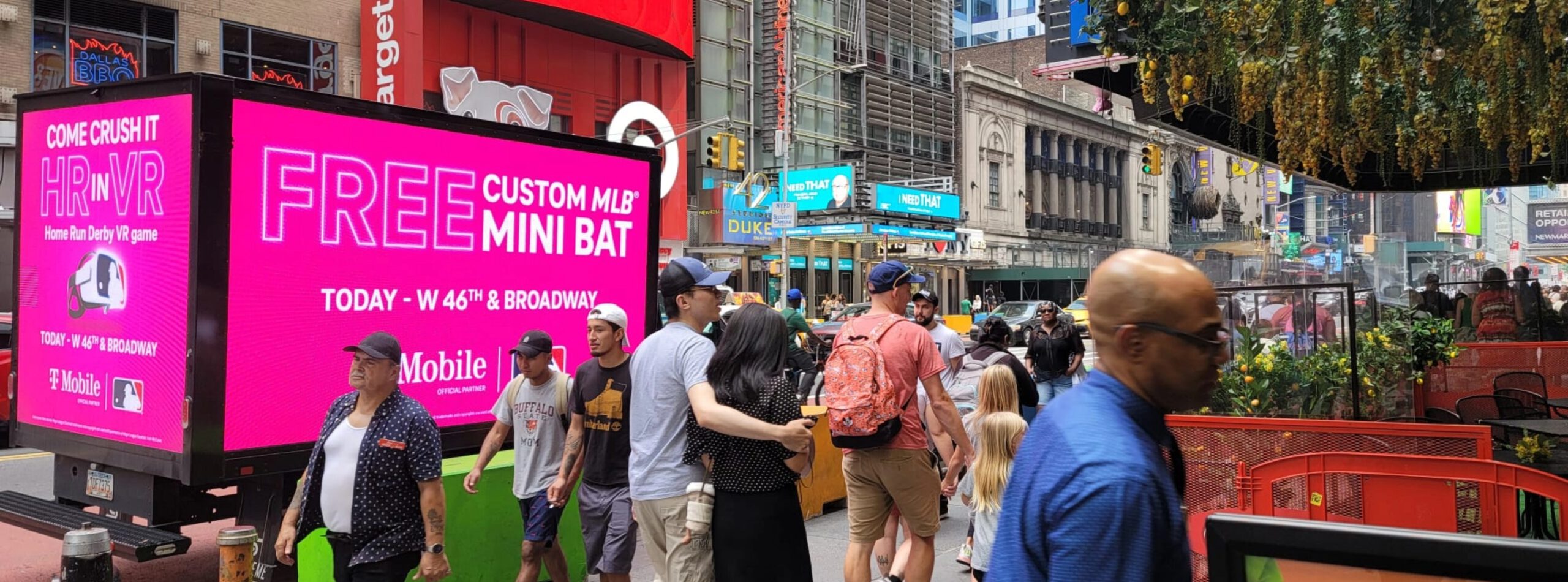 T-Mobile advertisement displayed on digital billboards on a busy sidewalk in New York City