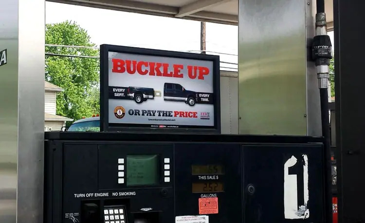 "Buckle Up" PSA poster atop a gas pump