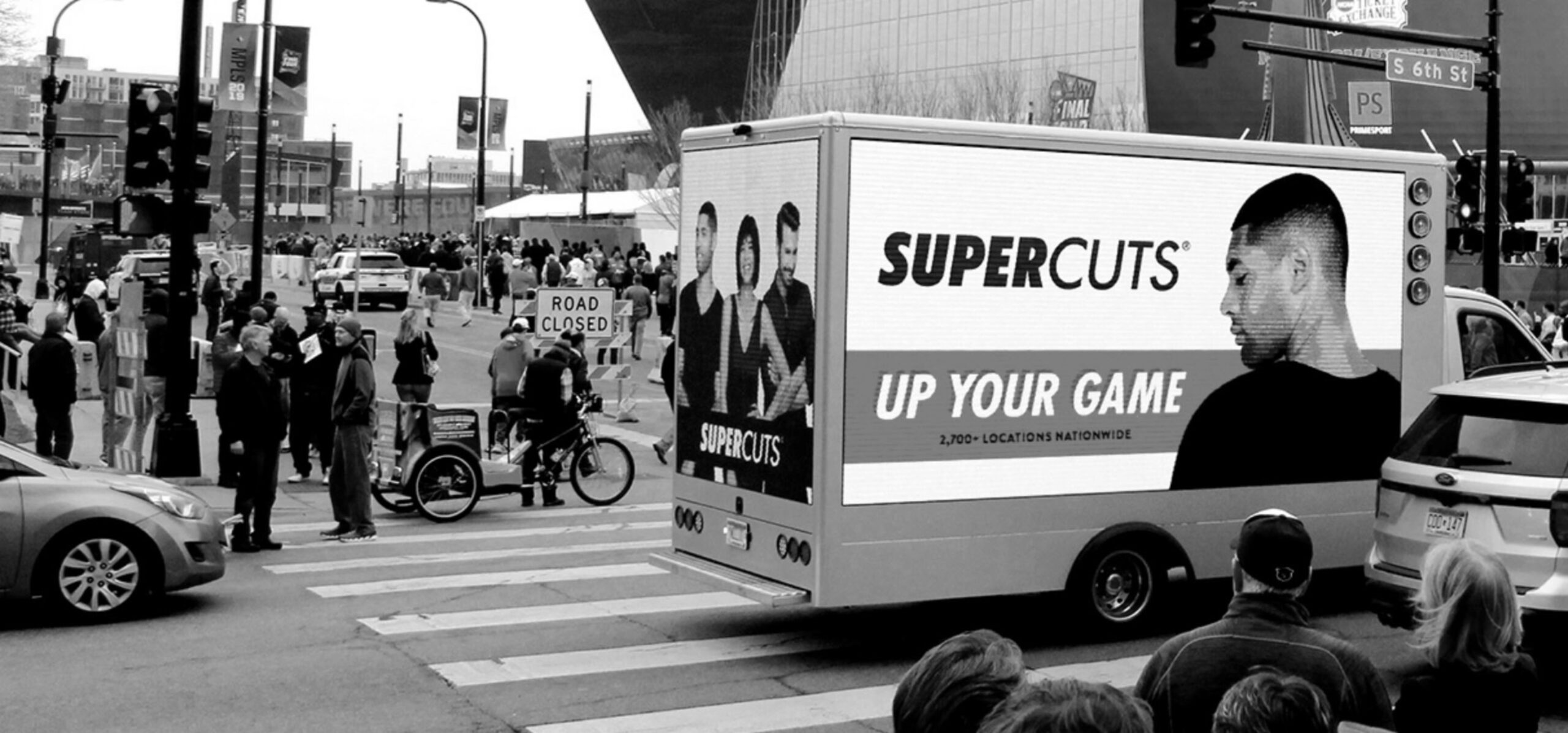 Black and white image of a truck in traffic that displays a SuperCuts ad on its side